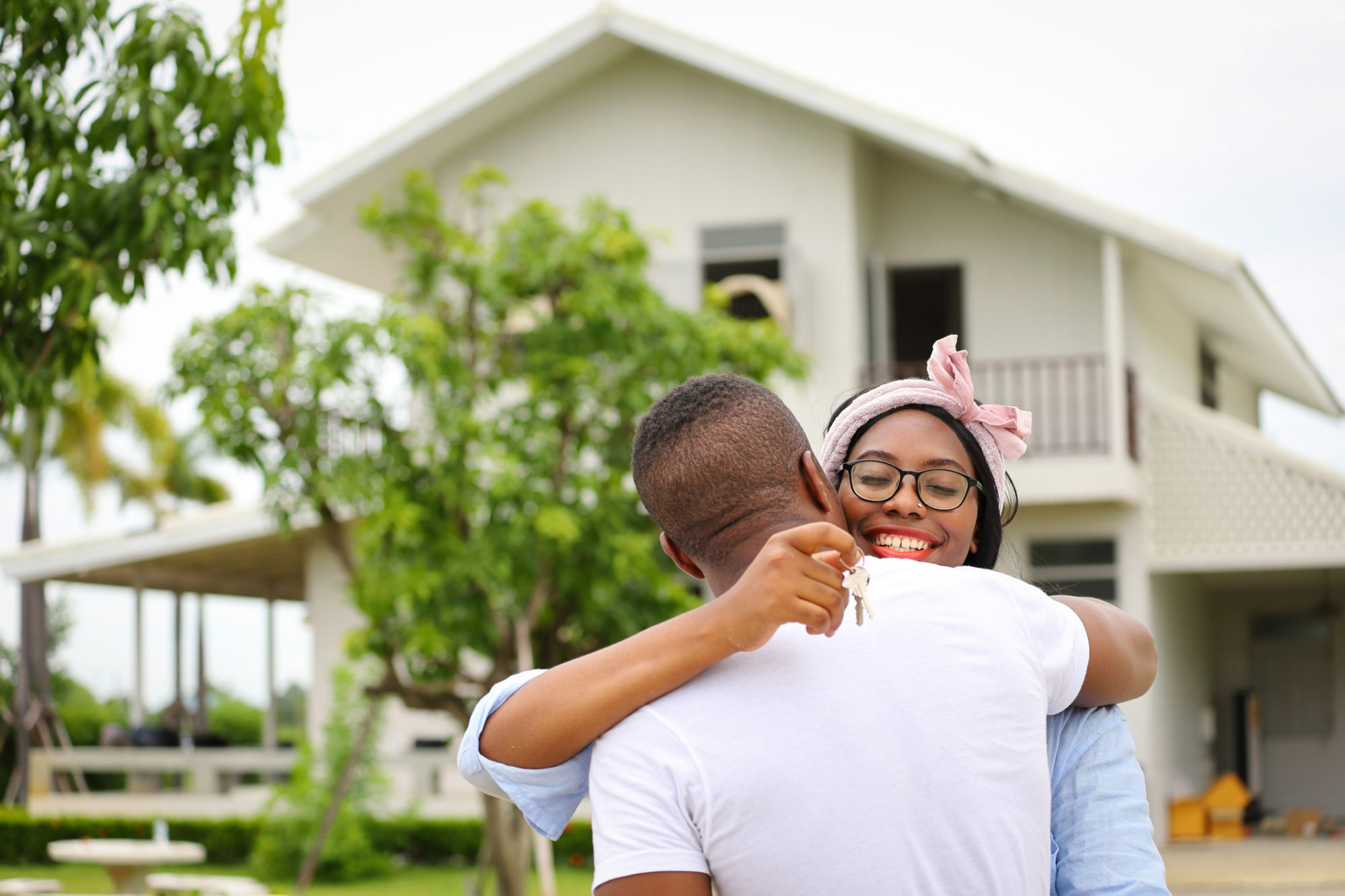 Wife hugging her husband in front of the house they just move in while holding key for housing, relocation and new family